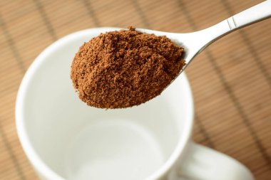 Kahverengi bambu arka planına karşı beyaz boş bardağın üzerinde öğütülmüş kahve kaşığı.