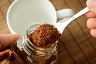 Kahve kavanozundan öğütülmüş kahve alan adam. Boş bardak kahverengi arka planda duruyor. Kahve yapıyorum.