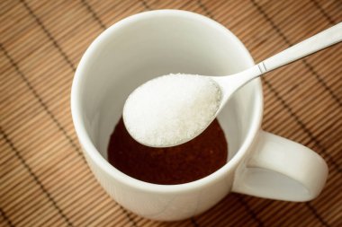Holding sugar over the cup with coffee. Adding sugar to the coffee. Making coffee at home