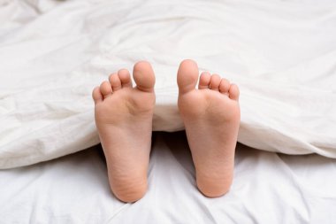 Child`s bare feet from under the cover while sleeping