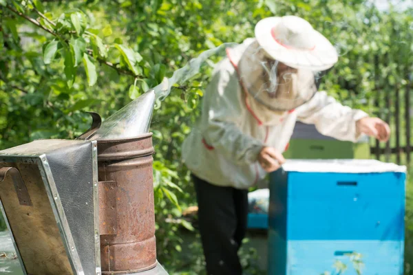 Bee smoker tool against the beekeeper with beehives