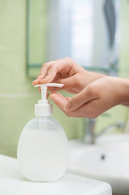 Çocuk el yıkamadan önce plastik şişeden sıvı sabun alıyor.