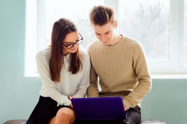 Koridordaki pencerenin yanında oturan genç öğrenciler modern dizüstü bilgisayarlarını kullanarak ortak projeleri üzerinde çalışıyorlar. Çalışkan öğrenciler modern teknolojileri kullanarak birlikte çalışıyorlar.