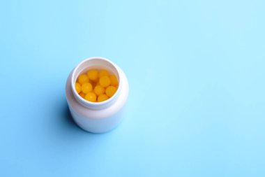 İçinde sarı top hapları olan beyaz plastik bir şişe. Üzerinde reçeteli haplar olan şişe mavi masada duruyor.