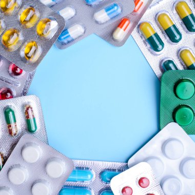 Concept of medicine. Frame of pills and capsules in blisters with a copy space for inscription in the middle on the blue table