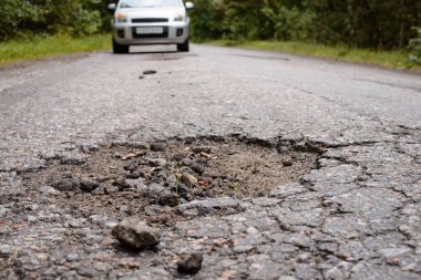 Road needs repairing. Countryside road with big pothole and car coming in the background