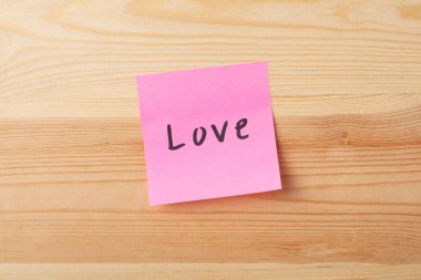 Ahşap bir arka planda pembe yapışkan bir notla yazılmış bir aşk.