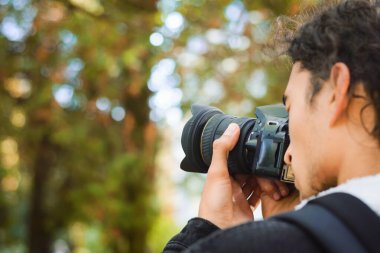 Genç bir gazeteci, bir sonbahar günü parkta yeni makalesi için fotoğraf çekiyor. Uzayı sola kopyala.