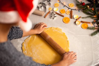 Mutfakta merdanenin yardımıyla hamuru yuvarlayan genç bir kızın arka görüntüsü. Noel akşamı için bisküvi pişiriyorum.