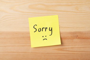 Yellow sticky note with inscription SORRY on wooden table