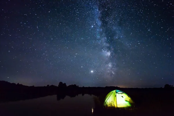 Night landscape of Milky Way and a tent on the foreground near the river. Concept of traveling