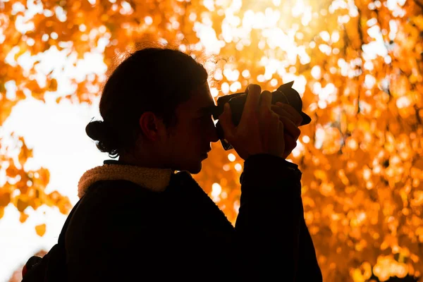 Güz manzaraları çeken, kameralı yakışıklı, genç profesyonel fotoğrafçı. Arka planda muhteşem altın ağaç dalları.