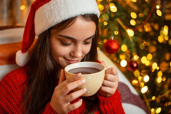 반바지를 크리스마스 모자를 코코아를 마시는 매력적 미소짓는 소녀의 모습을 십시오 — 스톡 사진