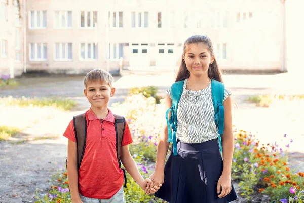 Two cheerful school pupils with backpacks standing in front of entrance of school. Back to school concept