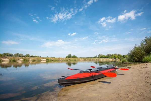 Big red canoe standing on the river shore with two paddles