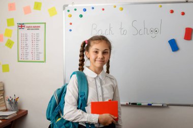 Sırt çantası ve kitabı olan güzel bir kız öğrenci okula geldi. Uzun bir tatilden sonra okula dönme kavramı