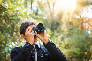Bright sun in the forest, beautiful nature in autumn. Young male photographer in black coat shooting trees, birds and sky.