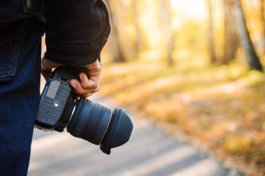 Man tourist walking in the park with camera in the hand. Nice sunny weather in early autumn, perfect time for travelling or small tour in nature, copy space.