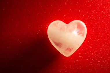Symbolic photo of transparent stone in shape of a heart on red background. Beautiful amolet for people in love