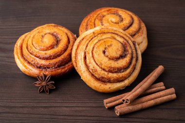 Three cinnamon buns on wooden table with some cinnamon sticks. Tasty homemade bakery