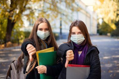Two dissatisfied students showing thumbs down to the camera. Senior students unhappy because of all the safety rules in the university while pandemic