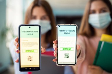 Close-up photo of two university students showing apps with digital vaccination certificate to the camera. Coronavirus vaccination concept