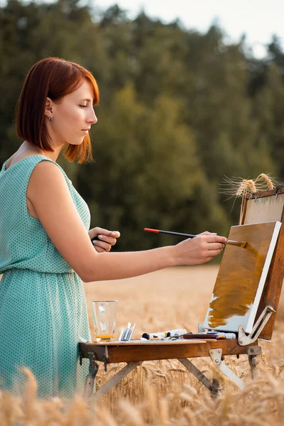 Concentrated painter girl applying oil paint to the canvas, drawing background of the painting. Young girl drawing a beautiful scene of field of wheat