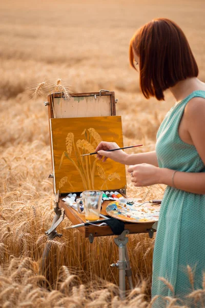 Back view of a professional artist painting spikelets of ripe wheat in the agricultural field. Painter at work