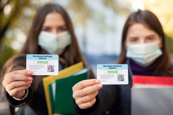 Two students showing vaccination certificates cards to the camera, focus on certicites. Concept of coronavirus vaccination among students
