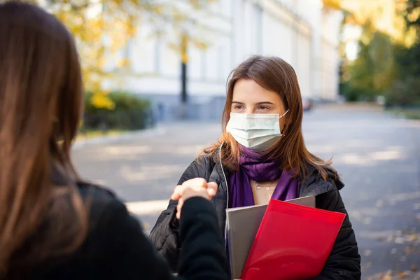 Happy students in medical masks greeting each other with their fists. Greeting while Covid-19 pandemic