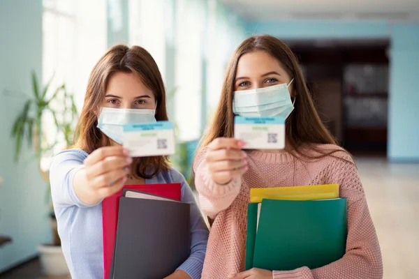 University students in protective medical masks with vaccination certificates in their hands. Concept of obligatory vaccination of students and teaching stuff