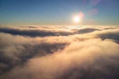 Aerial view of fluffy clouds with a sun on the horizon. Flying above the clouds