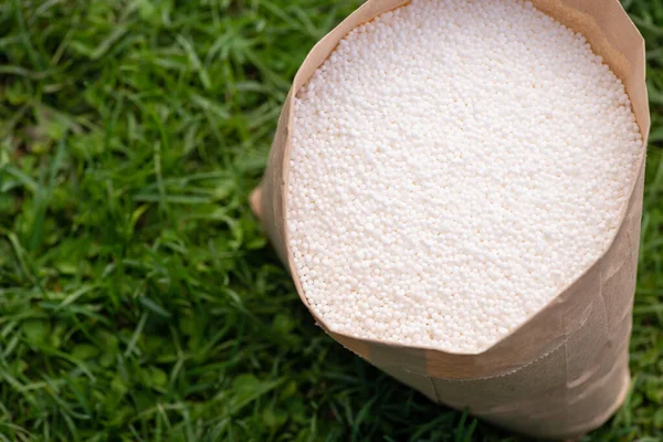 Close-up shot of fertilizer in bag standing on grass. Fertilizing lawn concept