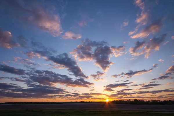 Panorama of setting sun over agricultural field, bright clouds lit by last sun rays in the sky