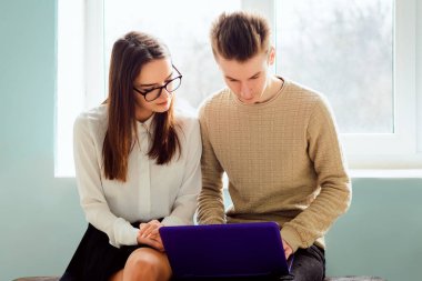 Üniversite molasında modern dizüstü bilgisayarı olan iki öğrenci. Çalışkan öğrenciler kampüsün penceresinin yanındaki bankta oturup bazı sorunları tartışıyorlar.