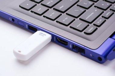 Beyaz bir masadaki modern mavi dizüstü bilgisayarın USB portuna takılı beyaz USB çubuğu
