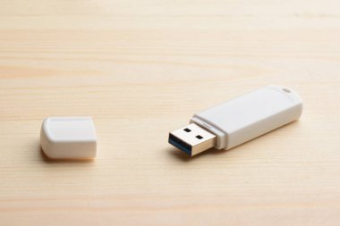 Hafif ahşap bir masada kapaklı beyaz USB çubuğu.
