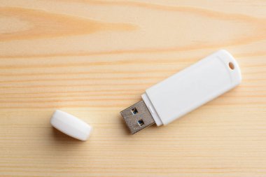 Hafif ahşap bir masada kapaklı beyaz USB çubuğu.
