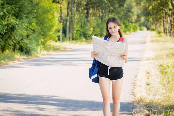 Attractive student girl traveling on summer holidays searching direction on location map while traveling in the countryside