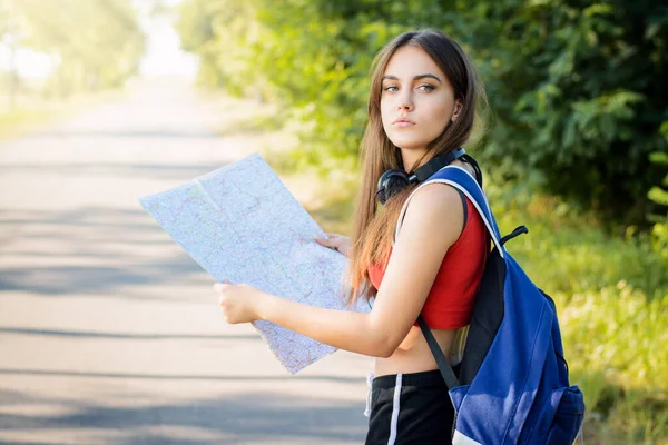 Female tourist with a map and heavy backpack looking back while traveling in the forest in the evening