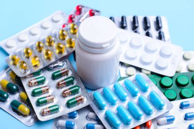 Farklı boylarda ve renkte haplar ve kapsüller. Ortasında beyaz plastik bir şişeyle su toplamış.