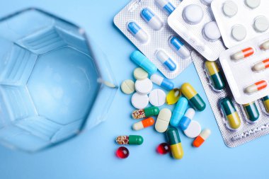 Farklı boyutlarda ve renkte haplar folyoya sarılıp mavi arka plandaki su camının yanına yerleştirilmiş.