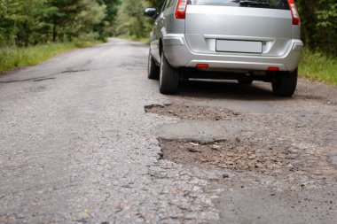 Bir sürü çukur olan kırsal yolda giden modern bir arabanın arkası.