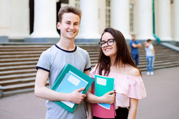Двое друзей стоят у здания университета на открытом воздухе с книгами и учебниками перед занятиями