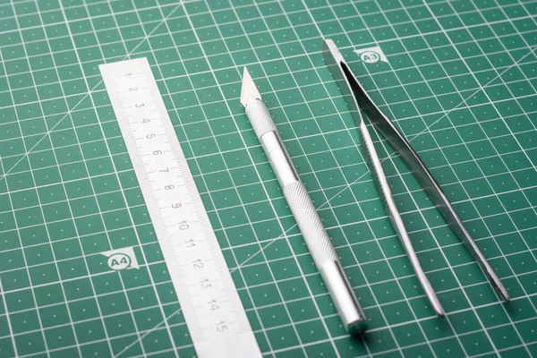 Stationery equipment on a cutting mat. Ruler, scalpel or knife; tweezers on a green cutting mat