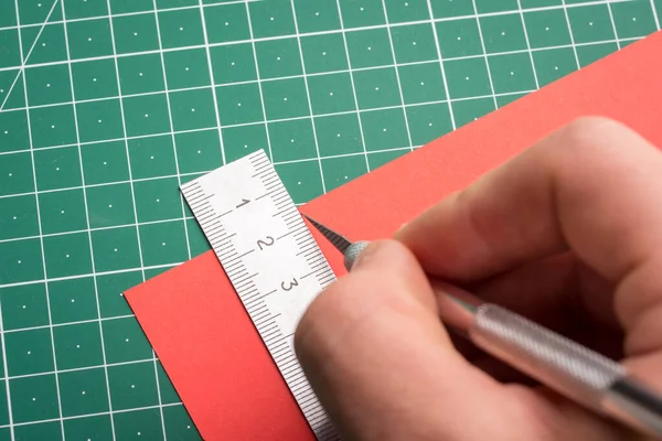 Male cutting red paper with a help of paper scalpel; ruler and cutting mat