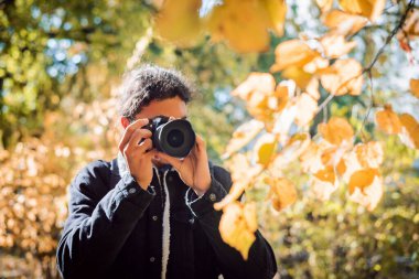 Şehir parkında sonbahar yaprakları çeken amatör bir fotoğrafçı.