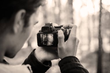 Parkta fotoğraf ve video çeken bir erkek kameramanın siyah beyaz fotoğrafı.