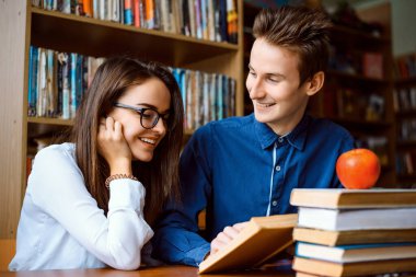 Öğrenciler kütüphanede birlikte araştırma yapar, okurlar, gülerler, araştırmalarının konusunu tartışırlar. Genç çift öğrenerek eğleniyor..