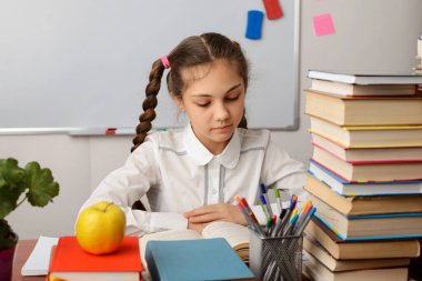 Genç ve güzel bir öğrenci kitap okuyor. İki örgülü beyaz bluzlu, konsantre olmuş küçük kız ödevlerini masada diğer bir çok öğrenme şeyiyle birlikte yapıyor..